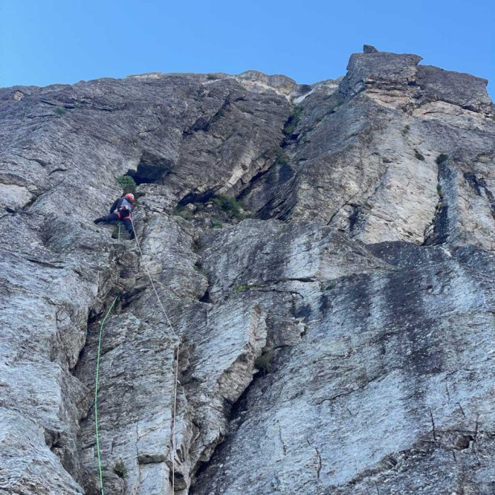 Arrampicatore fotografato dal basso su parete rocciosa frastagliata